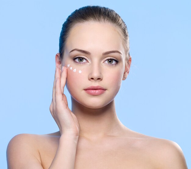 Retrato de joven adulta aplicando crema en la piel alrededor de los ojos en azul