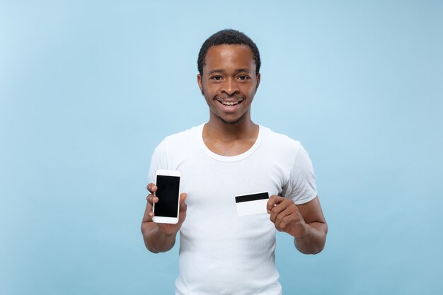 Retrato de joven afroamericano con camisa blanca sosteniendo una tarjeta y un teléfono inteligente.