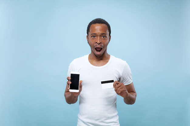 Retrato de joven afroamericano con camisa blanca sosteniendo una tarjeta y un teléfono inteligente.