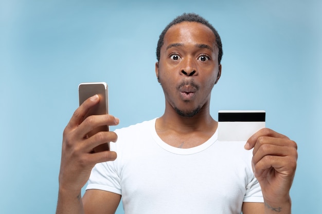 Retrato de joven afroamericano con camisa blanca sosteniendo una tarjeta y un teléfono inteligente.