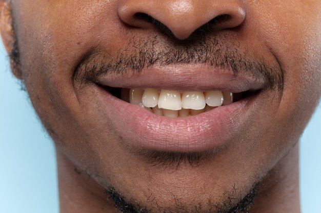 Retrato de joven afroamericano en pared azul de cerca. Las emociones humanas, la expresión facial, el anuncio, las ventas o el concepto de belleza. sesión de fotos de labios. Parece tranquilo, sonriente, mostrando los dientes.