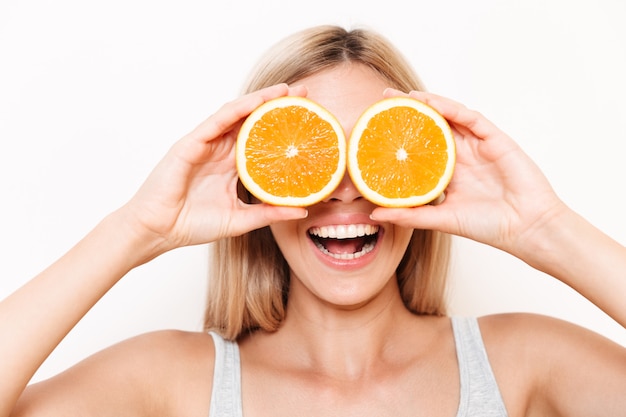 Retrato de una joven alegre que cubre sus ojos con fruta naranja