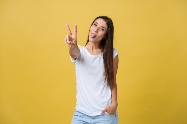 Retrato de una joven alegre que muestra dos dedos o un gesto de victoria sobre un fondo amarillo