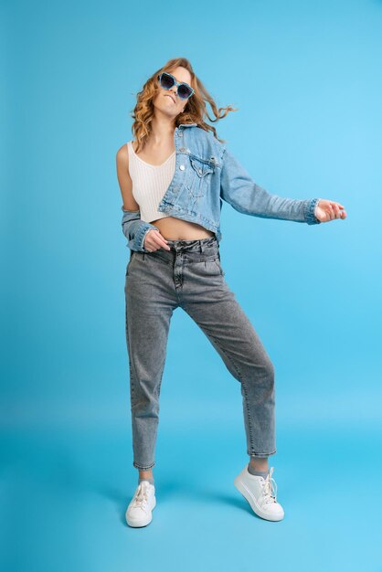 Retrato de una joven alegre con ropa informal bailando posando aislada sobre el fondo azul del estudio