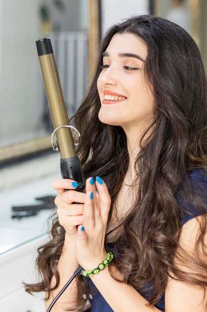 Retrato de una joven alegre sosteniendo un secador de pelo con ambas manos y sonriendo