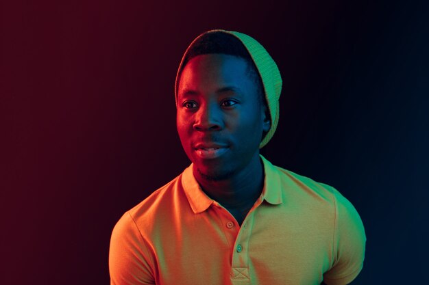 Retrato de un joven americano feliz sonriendo contra la pared del estudio de neón negro de cerca