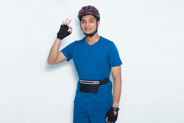 Retrato joven apuesto ciclista asiático mostrando el pulgar hacia arriba gesto ok aislado sobre fondo blanco.