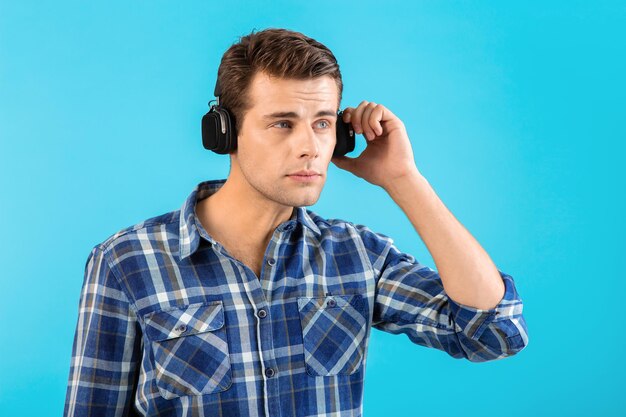 Retrato de un joven apuesto y elegante que escucha música con auriculares inalámbricos y se divierte con un estado de ánimo emocional feliz de estilo moderno aislado en un fondo azul con pantalones a cuadros