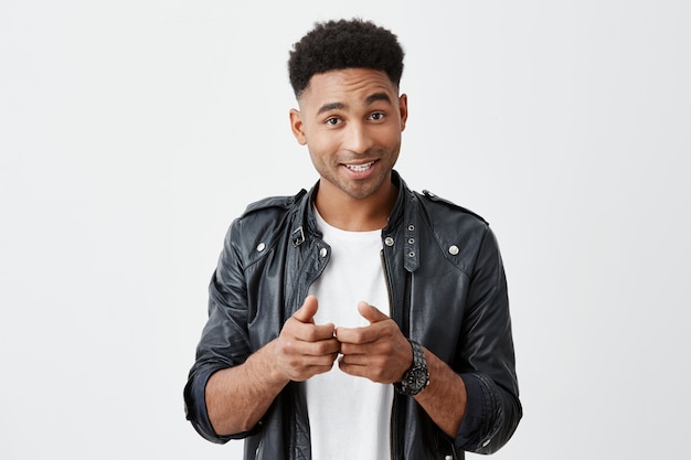 Retrato de joven apuesto estudiante de piel bronceada con peinado afro en traje casual elegante gesticulando con las manos, mostrando a su amigo que quiere jugar juegos de consola en el tiempo libre.