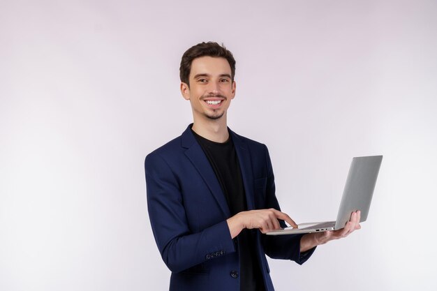 Retrato de un joven apuesto hombre de negocios sonriente sosteniendo una laptop en las manos escribiendo y navegando por páginas web aisladas de fondo blanco