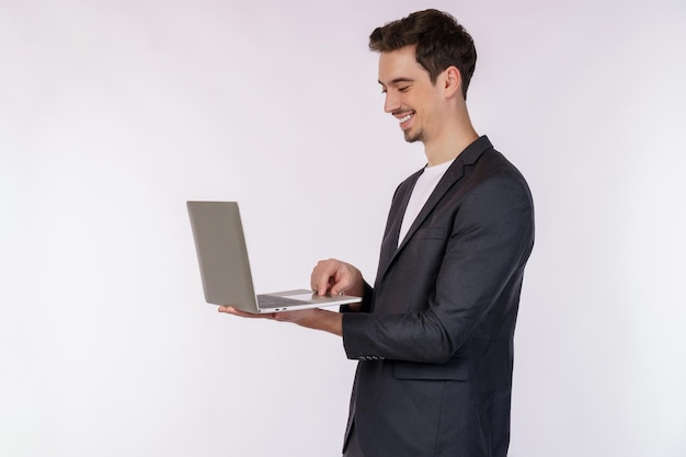 Retrato de un joven apuesto hombre de negocios sonriente sosteniendo una laptop en las manos escribiendo y navegando por páginas web aisladas de fondo blanco