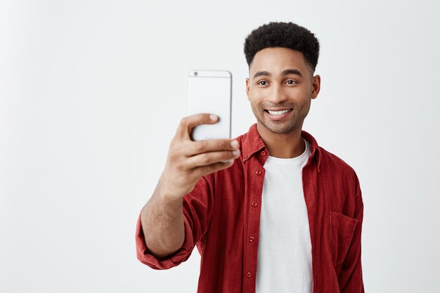 Retrato de joven apuesto hombre de piel morena con peinado afro en traje casual de moda sonriendo con dientes, tomando fotos de amigos durante las vacaciones.