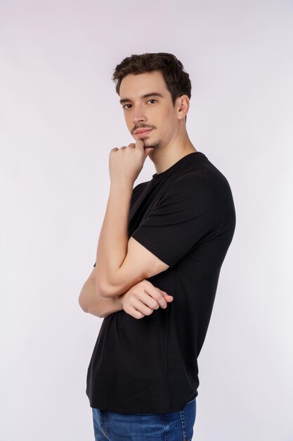 Retrato de un joven apuesto que mira confiado a la cámara con una sonrisa con los brazos cruzados y la mano levantada en la barbilla sobre un fondo aislado