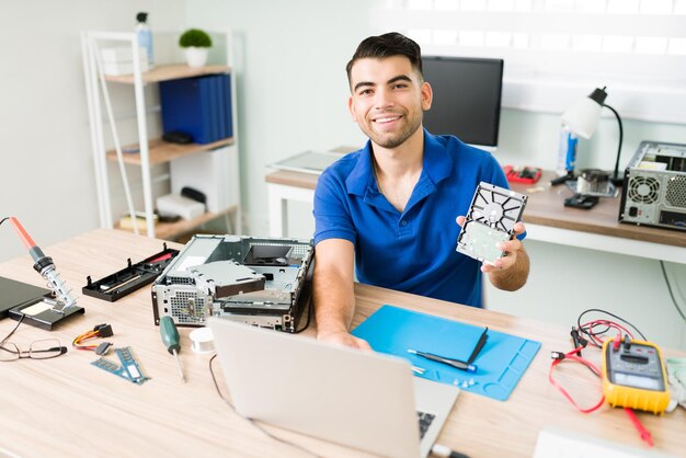 Retrato de un joven apuesto que sonríe mientras hace una copia de seguridad de datos en una computadora portátil y trabaja en soporte técnico