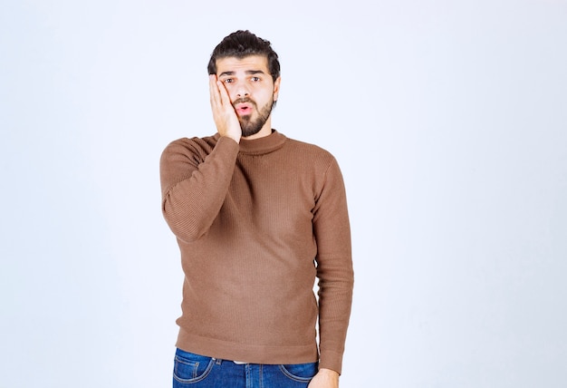 Retrato de un joven apuesto en suéter casual sosteniendo la palma cerca de la mejilla.