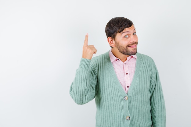 Foto gratuita retrato de joven apuntando hacia arriba en camisa, chaqueta de punto y mirando alegre vista frontal