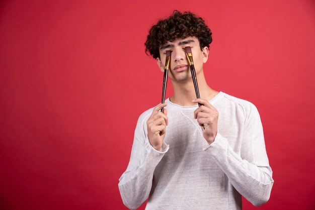 Retrato de un joven artista masculino cerrando los ojos con pinceles.