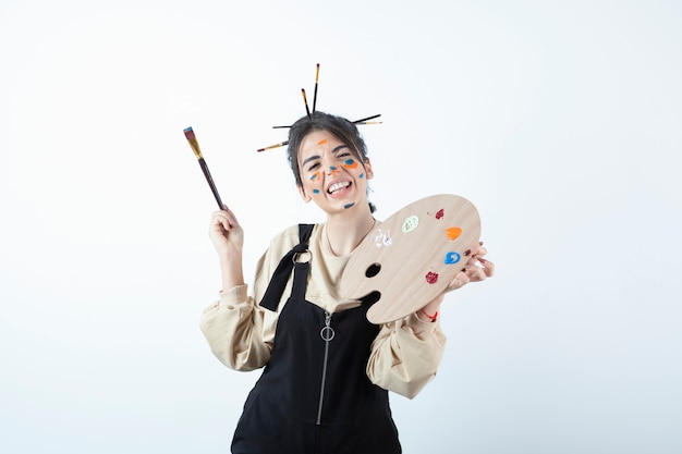 Retrato de una joven artista posando con la cara pintada y sosteniendo la paleta de madera.