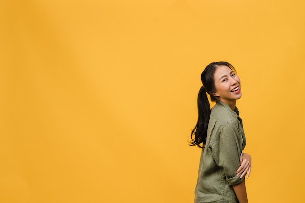 Retrato de joven asiática con expresión positiva, sonrisa amplia, vestida con ropa casual sobre pared amarilla. Feliz adorable mujer alegre se regocija con el éxito. Concepto de expresión facial.