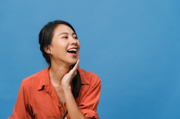 Retrato de joven asiática con expresión positiva, sonrisa amplia, vestida con ropa casual sobre pared azul. Feliz adorable mujer alegre se regocija con el éxito. Concepto de expresión facial.