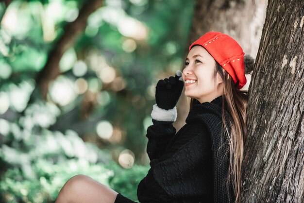 Retrato de una joven asiática feliz sentada en un césped bajo un árbol en el parque Concepto de cuidado del medio ambiente