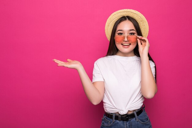 Retrato de una joven asiática en gafas de sol en pared rosa