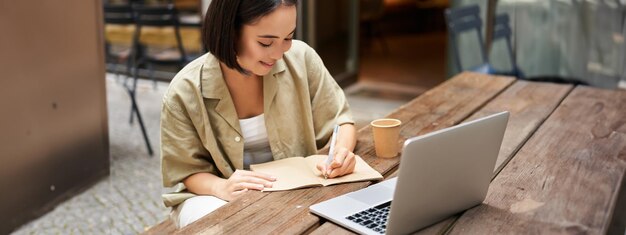 Retrato de una joven asiática que trabaja en una computadora portátil tomando notas mientras asiste en línea