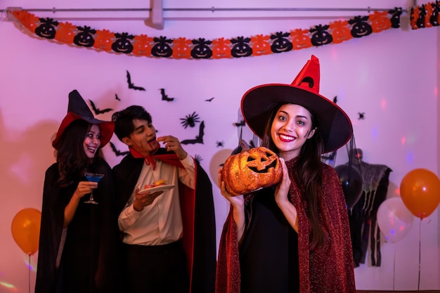 Retrato de una joven asiática sonriendo en un disfraz de Halloween como bruja en calabaza de fiesta o Jack O Lantern mirando a la cámara