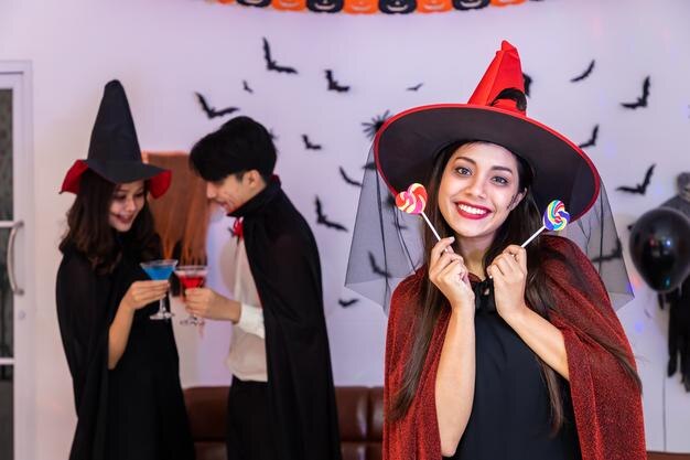 Retrato de una joven asiática sonriendo en un disfraz de Halloween como bruja en una fiesta sosteniendo dulces mirando la cámara