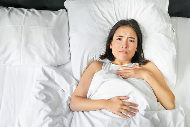 Retrato de una joven asiática triste acostada en la cama pensando demasiado antes de irse a dormir hasta tarde porque