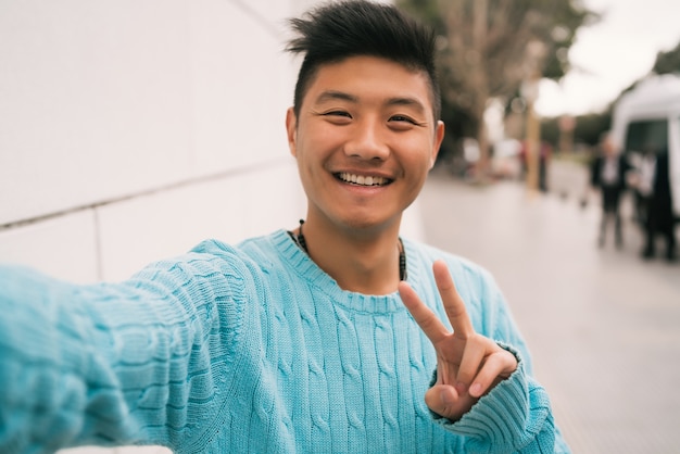 Retrato de joven asiático mirando confiado y tomando un selfie mientras está de pie al aire libre en la calle.
