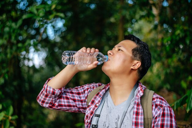 Retrato joven asiático trekking bebe agua de una botella de plástico durante el descanso en el espacio de copia del sendero del bosque