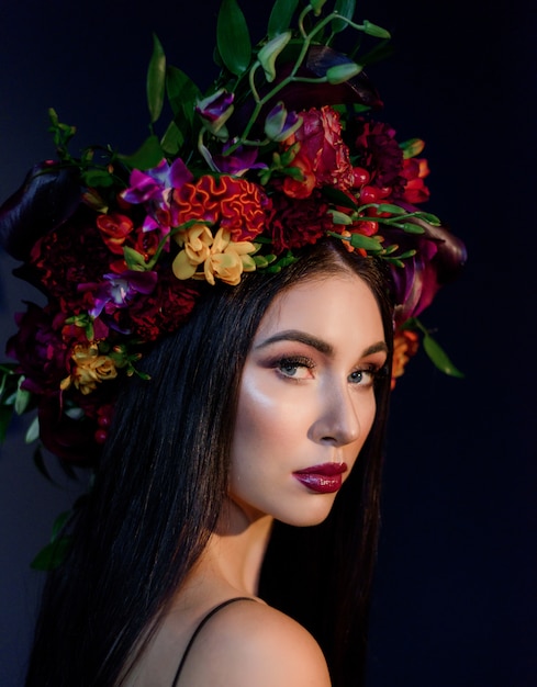 Retrato de joven atractiva con maquillaje brillante vestida con una gran corona floral colorida