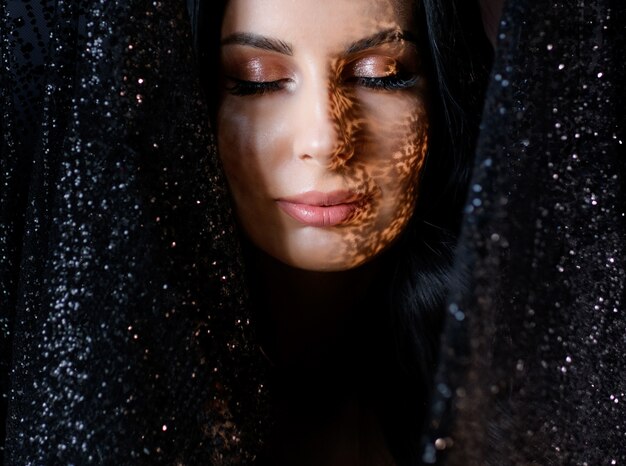 Retrato de joven atractiva con maquillaje tierno y sombra en la cara rodeada de encaje negro brillo