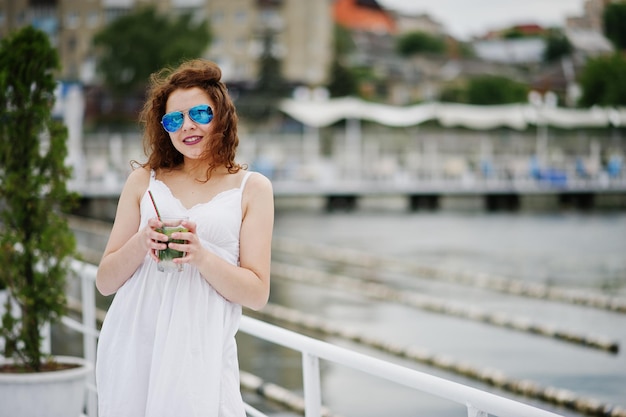 Foto gratuita retrato de una joven atractiva posando con su cóctel en un lago con gafas de sol