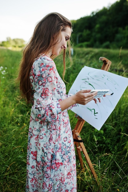 Retrato de una joven atractiva con un vestido largo pintando con acuarela en la naturaleza