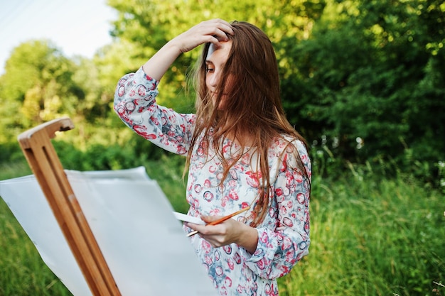 Retrato de una joven atractiva con un vestido largo pintando con acuarela en la naturaleza