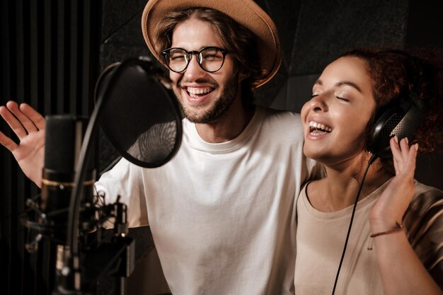 Retrato de un joven y atractivo hombre y una mujer cantando felizmente juntos en un moderno estudio de grabación de sonido
