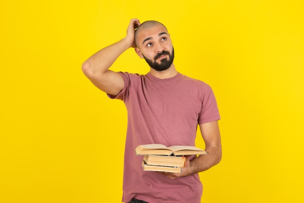 Retrato de un joven barbudo sosteniendo libros sobre pared amarilla.