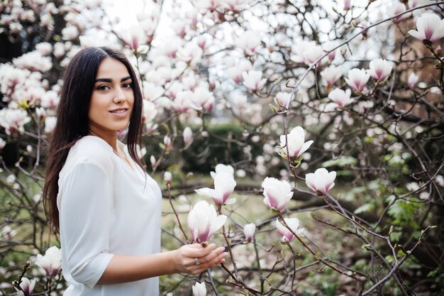 Retrato de una joven bella dama cerca del árbol de magnolia con flores.