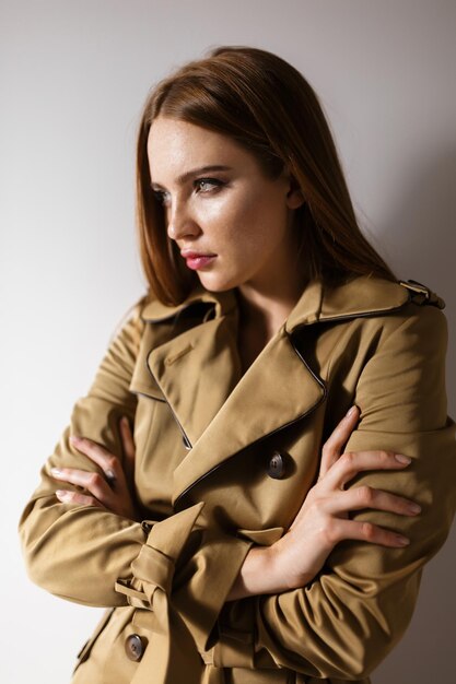 Retrato de joven bella dama en gabardina de pie y mirando cuidadosamente a un lado