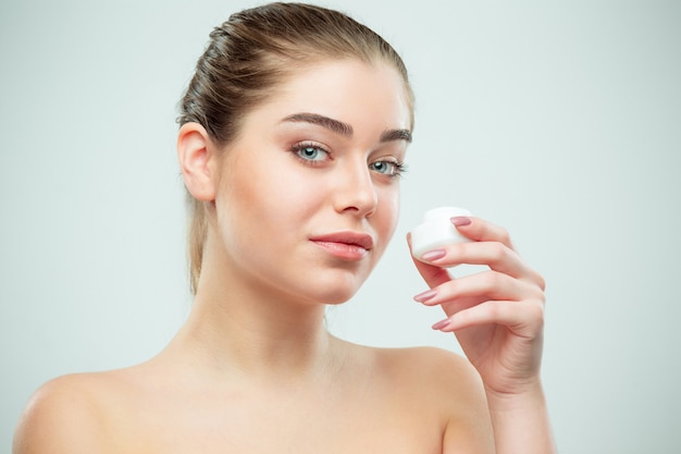 Retrato de joven bella mujer aplicando crema hidratante en la cara