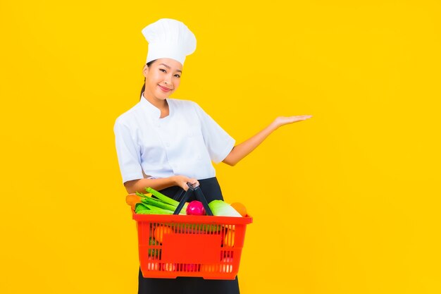Retrato joven y bella mujer asiática chef con canasta de supermercado sobre fondo amarillo aislado