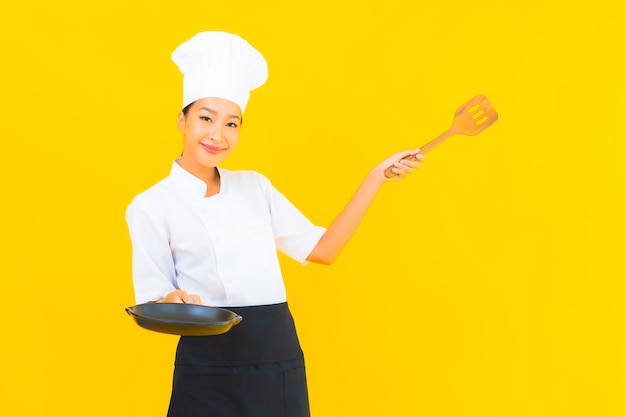 Retrato joven y bella mujer asiática chef con espátula sobre fondo amarillo aislado