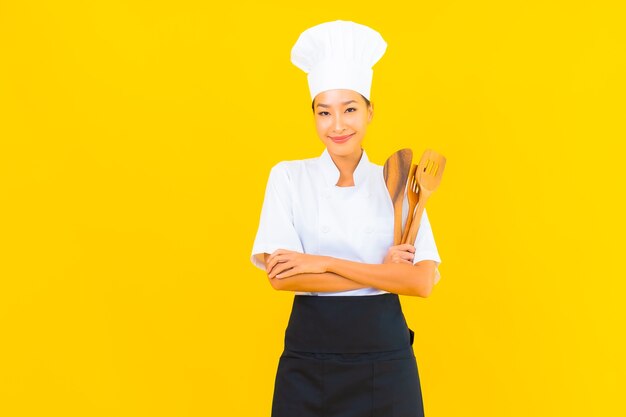 Retrato joven y bella mujer asiática chef con espátula sobre fondo amarillo aislado