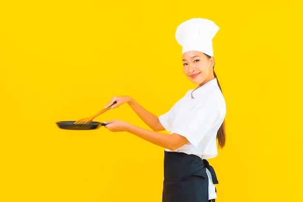 Retrato joven y bella mujer asiática chef con pan negro sobre fondo amarillo aislado