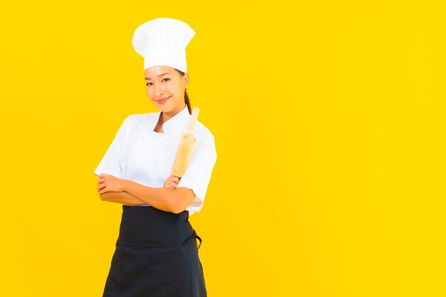 Retrato joven y bella mujer asiática chef con rodillo sobre fondo amarillo aislado