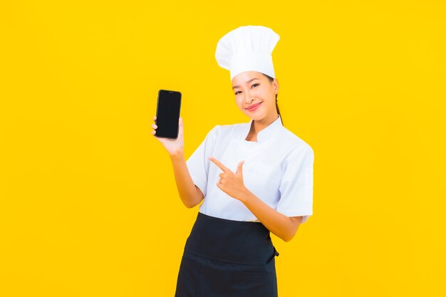 Retrato joven y bella mujer asiática chef con teléfono móvil inteligente sobre fondo amarillo aislado