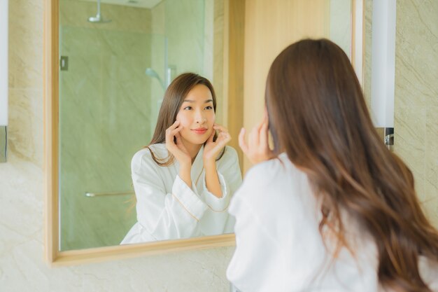 Retrato joven y bella mujer asiática chequeo cara en el baño.