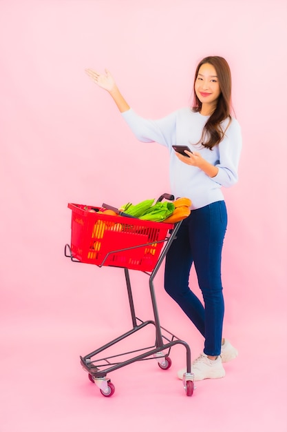 Retrato joven y bella mujer asiática con frutas y verduras y abarrotes en la canasta en la pared aislada rosa